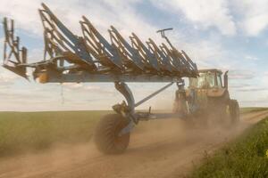 A tractor is diligently plowing a vast green field as the sun begins to set, creating a picturesque view with scattered clouds in the sky photo
