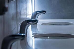 Sleek faucets are shown in a stylish restroom featuring polished surfaces and a minimalist aesthetic, creating a contemporary and clean atmosphere photo