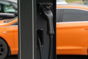 Close view of an electric vehicle charging station showcasing a connector in use, with a bright orange car parked nearby in a modern urban setting photo