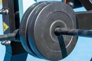 Close-up view of heavy weight plates secured on a barbell in an outdoor gym setup, ready for a rigorous workout session under clear blue skies photo