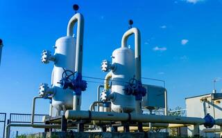 Two large gas processing units with valves and piping stand prominently against a bright blue sky at a manufacturing site during the day photo