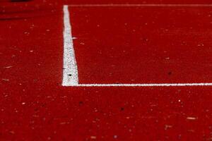 A vibrant red running track features a precise white line marking a lane boundary. Various debris is visible on the surface, indicating recent activity photo