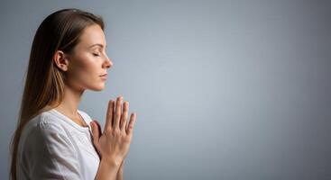 Medium portrait of a young woman with eyes closed and hands behind her head in a prayerful, meditative pose. Peaceful expression reflects faith and inner calm. photo