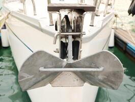 Close-up view of a modern yacht anchor mounted at the bow, docked in clear greenish water. Nautical equipment detail with visible textures and reflections. photo