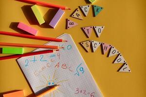 Back-to-school composition with pencils, sticky notes, and a math notebook on yellow background. Wooden bunting spells BACK TO SCHOOL colorful and fun. photo