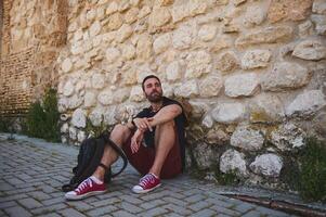 Man Resting Against Historical Stone Wall Amidst a Scenic Urban Setting photo
