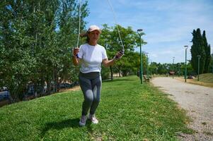 Middle-Aged Woman Exercising Outdoors by Skipping Rope in a Sunny Park Setting photo