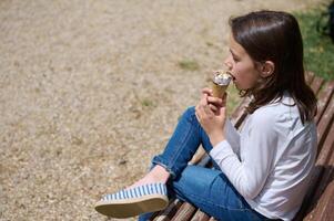 Young Girl Enjoying Ice Cream on a Park Bench in Sunny Weather photo