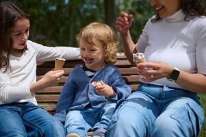 Family Enjoying Ice Cream Together on a Park Bench in the Sun photo