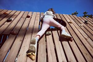 Rear View of a Child Climbing a Wooden Wall on a Sunny Day photo