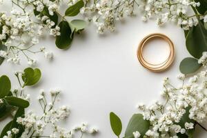 Wedding rings resting on white background surrounded by eucalyptus leaves and gypsophila flowers photo