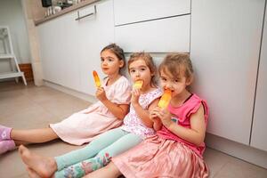 Three joyful girls enjoying colorful ice pops indoors photo