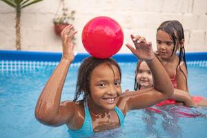 Children enjoying a sunny day playing with a red ball in a pool photo