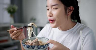Handheld selective focus shot, Young woman is happy to have delicious noodles for lunch on the table at home. Enjoying hot pot noodles. video