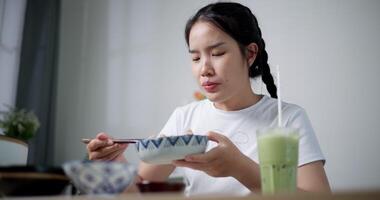 Handheld shot, Young Asian woman is happy to have delicious noodles for lunch on the table at home. Enjoying hot pot noodles. video