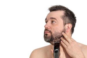 Handsome young man using an electric razor to shave his facial hair. The man is focused and intent as he grooms himself against a clean white background. photo
