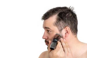 Close-up of a young man shaving his face with an electric razor, isolated on a white background. The man is focused and engaged in his grooming routine. photo