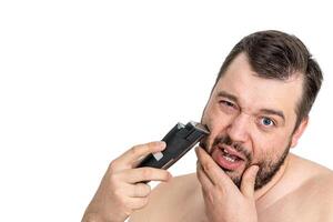 Isolated shot of a young man grooming with an electric razor on a white background. The man appears focused and the image reflects personal care and grooming. photo