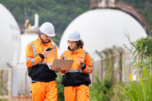 Engineers Collaborating at Industrial Site with Storage Tanks, Team of Engineers Conducting Operations at Oil Storage Field Industrial Site, Industrial Workers Communicating and Using Laptop at Site photo