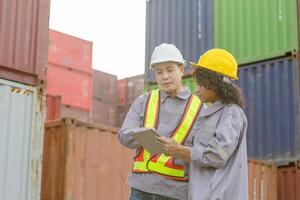Engineer and foreman worker team in hardhat and safety vest checking containers box from cargo, Engineers with tablet managing cargo operations, Teamwork concepts photo