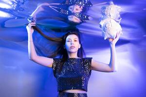 Girl Dressed as a Mermaid Glimmers Underwater While Holding a Seashell in Vibrant Blue Lighting photo