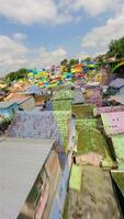 Cinematic FPV drone flythrough of rainbow-colored rooftops and river in vibrant village in Malang, Indonesia. Colorful houses, tropical atmosphere, and local life. video