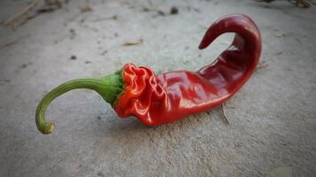 A single red chili pepper with a green stem lying on a gray surface in a close up shot view photo