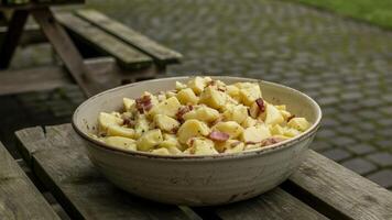A bowl of potato salad sitting on a wooden table photo