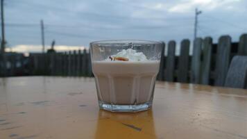 A glass of dessert with whipped cream and a topping on a yellow table with a cloudy sky behind it photo