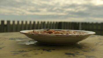 A close up of a bowl of beans on a table with a fence and cloudy sky in the background outdoors photo