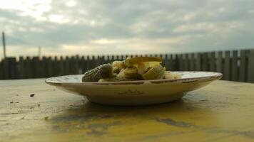 A plate of pickles and chopped vegetables on a yellow table with a cloudy sky in the background photo