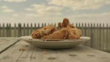 Close up of fried chicken on a plate sitting on a wooden table with a fence and sky background photo