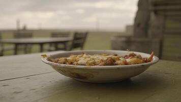 A bowl of food sits on a table outdoors with a blurred background on an overcast day outside photo