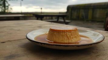 Caramel custard dessert on a plate sitting on a wooden table outside on a cloudy day in the distance photo