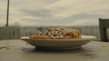 A plate of funnel cake topped with powdered sugar on a table outside with a cloudy sky background photo