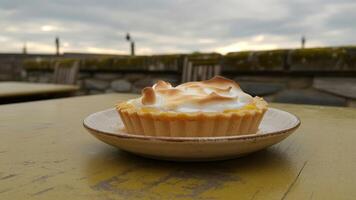 Lemon meringue tart on a plate outdoors with a cloudy sky in the background on a yellow table photo