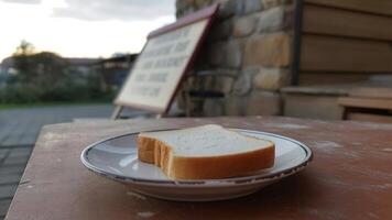 A slice of white bread on a plate sitting on a table outdoors with a building in the background photo