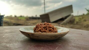 A plate of brown food sitting on a table with a blurry background of a cloudy sky and greenery photo