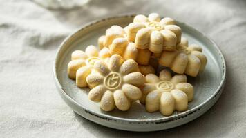 A plate of flower shaped cookies dusted with powdered sugar on a textured white surface close up view photo