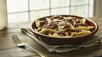 Close up of ravioli with tomato sauce in a brown bowl on a wooden table with a fork and linen cloth photo