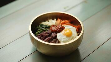 A close up of a bibimbap bowl with an egg and vegetables on a wooden surface in soft lighting photo