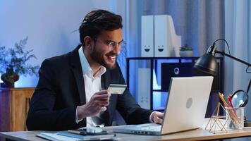 Arabian businessman programmer software developer working making online purchase payment shopping with credit bank card and use laptop at home office desk with laptop. Indian freelancer business man video