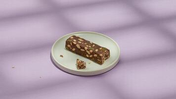 A chocolate nut bar on a white plate with a piece broken off against a purple background in soft light photo