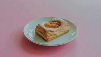 A close up of a pastry filled with orange jam on a white plate against a pink background space for text photo