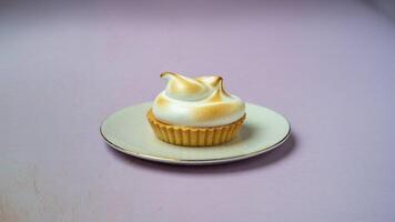 A single lemon meringue tartlet on a white plate with a gold rim on a lilac colored background photo