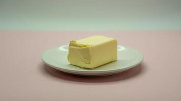 A block of butter sitting on a small white plate against a pink and white background in soft lighting photo