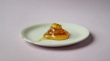 A close up of a white plate with a pile of golden honey against a light pink background studio shot photo
