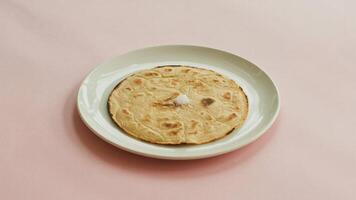 A roti with ghee on a white plate against a pink background in a simple and minimalist style image photo