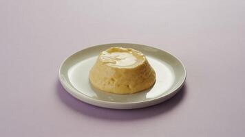 A caramel custard dessert on a white plate with a light purple background in a studio shot photo