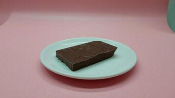 A rectangular piece of chocolate on a small white plate against a pink background in a studio shot photo